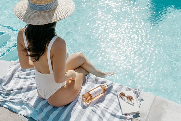 woman in white bikini lying on white and blue stripe towel on swimming pool during daytime